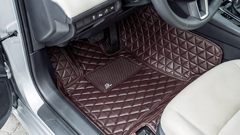 فرش أرضيات نمط ألماسي Diamond Floor Mats في الدمام – اسار أوتو | جلد بني فاخر فرش أرضية بجلد بني داكن بنمط ألماسي مبطن وشعار Glory تغطي أرضية السيارة بالكامل مع مقعد بيج في الخلفية.