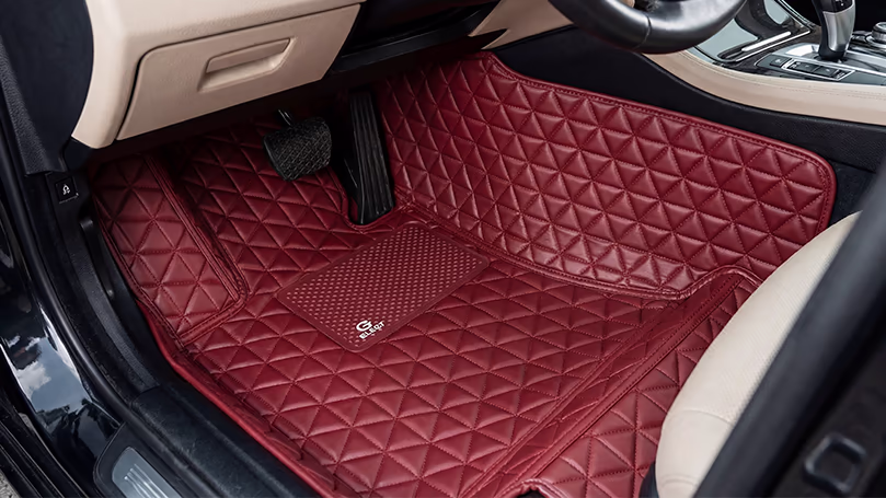 فرش أرضيات نمط مثلث Triangle Floor Mats في الدمام – اسار أوتو | جلد أحمر بتصميم مميز فرش أرضية بجلد أحمر داكن بنمط مثلثات مبطنة وشعار Glory تغطي أرضية السيارة بالكامل مع مقعد بيج في الخلفية.